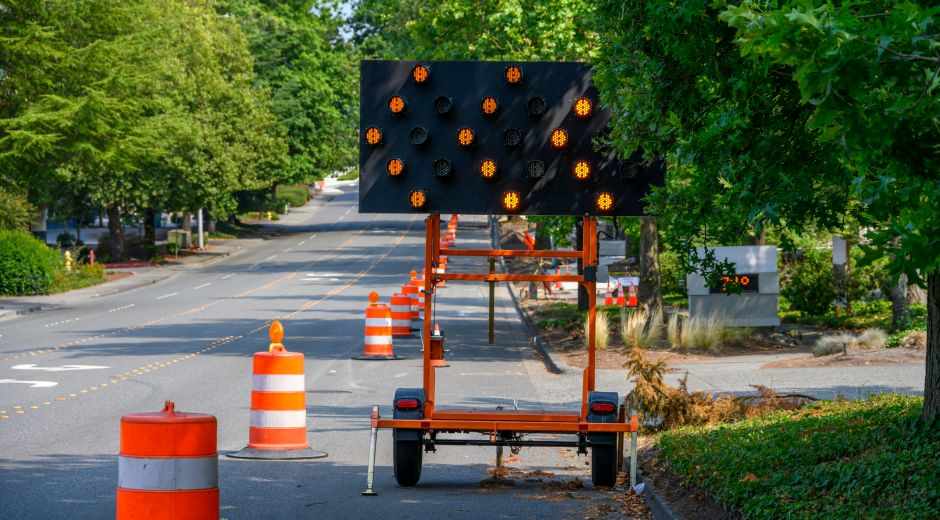 Portable arrow board trailer and orange traffic barrels set up for a traffic control business on a residential street.